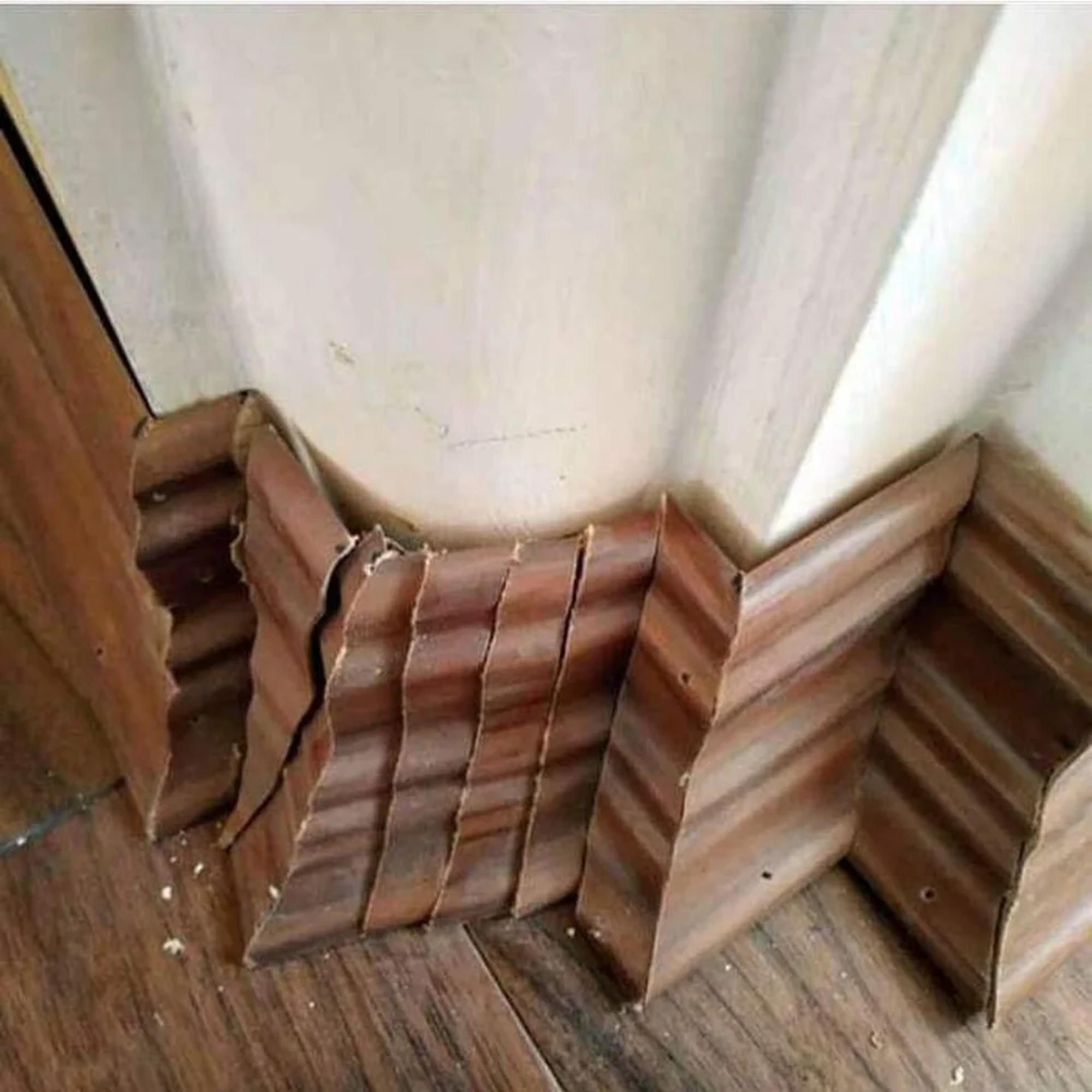 Een muur met hoekjes en een bocht met een plint. De plint is in allemaal losse stukjes in een vergeefse poging om de vorm van de muur te volgen.